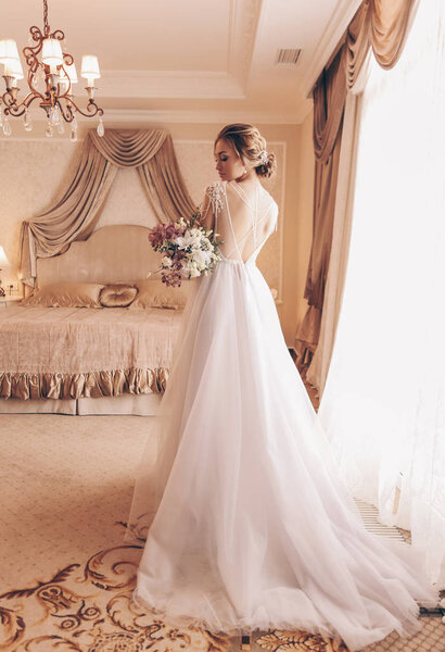 модный интерьер фото красивой женщины с светлыми волосами в роскошном свадебном платье и аксессуары
