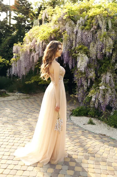 Kvinna med långt hår i lyxig klänning poserar bland blommande w — Stockfoto