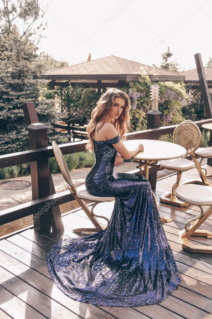 woman with long hair in luxurious dress sitting in outdoor cafe
