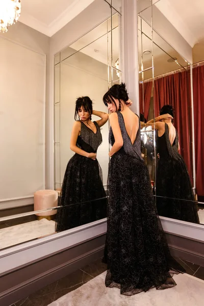 Beautiful woman with dark hair in elegant dress posing near mirr — Stock Photo, Image