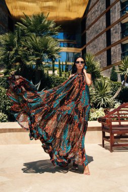 Güzel, siyah saçlı, şık elbiseli ve açık havada poz veren güzel bir kadının moda fotoğrafı.