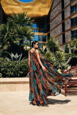 Güzel, siyah saçlı, şık elbiseli ve açık havada poz veren güzel bir kadının moda fotoğrafı.