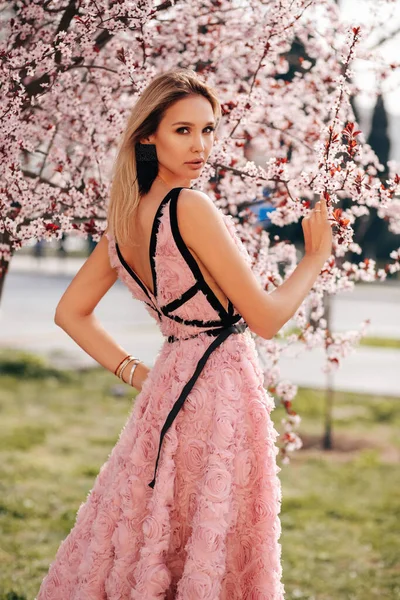 时尚的户外照片 美丽的性感女子 金发碧眼 穿着雅致的衣服 站在公园里盛开的桃树旁 — 图库照片