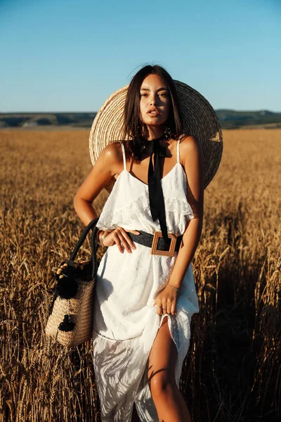 エレガントなドレスに黒い髪の美しい女性のファッション屋外写真や小麦の夏のフィールドの間でポーズ大きな麦藁帽子 — ストック写真