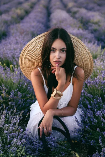 时尚的户外照片 美丽的女人 深色头发 穿着雅致的衣服 戴着大草帽 站在开着花的薰衣草场中间 — 图库照片