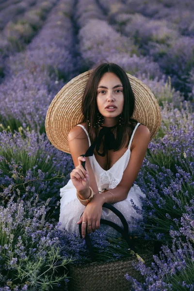时尚的户外照片 美丽的女人 深色头发 穿着雅致的衣服 戴着大草帽 站在开着花的薰衣草场中间 — 图库照片