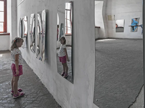 A girl looking at her image in the distorted mirror in the hall of mirrors — Stock Photo, Image