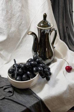 Bir siyah çaydanlık, üzüm ve beyaz dekoratif perdelik Olgun Kiraz ile natürmort