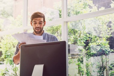 Bilgisayarın önündeki belgeler üzerinde çalışan meşgul bir adam