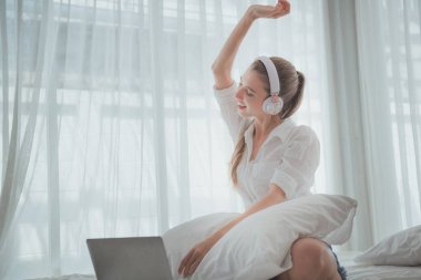 Güzel bir kadın çalışıyor ve yatağında müzik dinliyor.