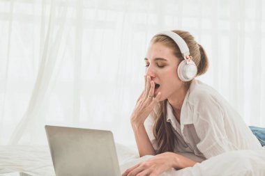 Yatakta dizüstü bilgisayar kullanan yorgun bir kadın.