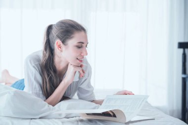 Genç ve güzel bir kadın evde uzanmış kitap okumaktan zevk alıyor..