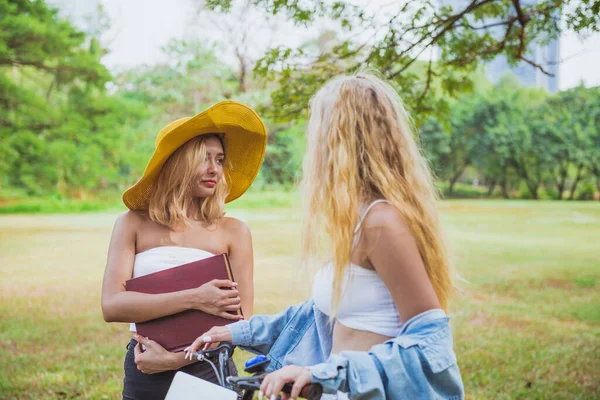 Beautiful women in conversation with friend while walking with bicycle at park