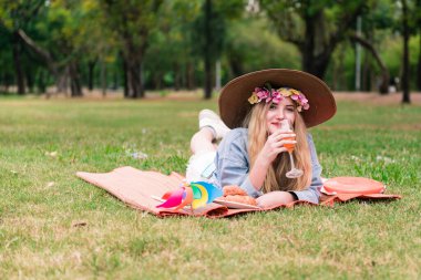 Tatlı bir kadın çimenlere uzanmış meyve suyu ve atıştırmalık içiyor.
