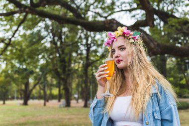 Güzel bir kadın elinde meşrubat bardağıyla parkta kola ya da bira içiyor.