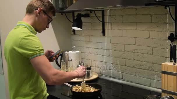Jonge man koken en messaging op mobiel — Stockvideo