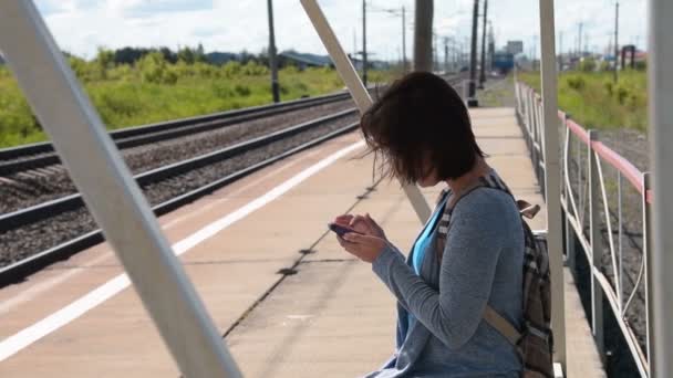 Donna che utilizza il cellulare in attesa di treno pendolare sul binario — Video Stock