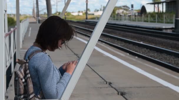 Женщина-путешественница с мобильным телефоном ждет поезда на платформе — стоковое видео