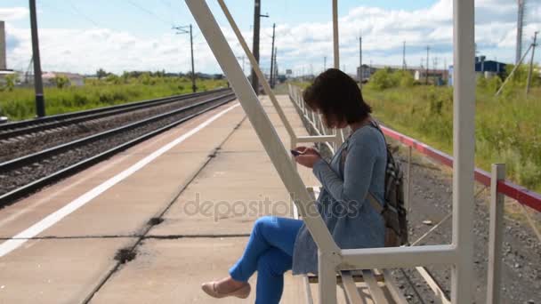 Žena používající mobilní při čekání na vlak dojíždějící na platformě — Stock video