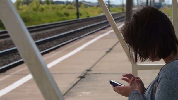 Mulher viajante com célula à espera de trem na plataforma — Vídeo de Stock