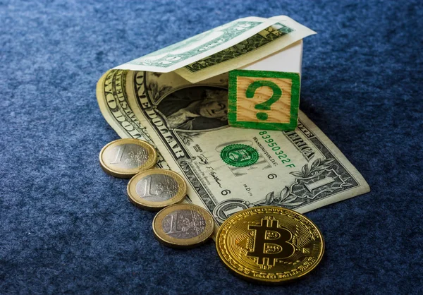Dolar banknotları ve Bitcoin ile Avro sikkeleri karanlık bir masa arkaplanında soru işareti olan bir küp ile