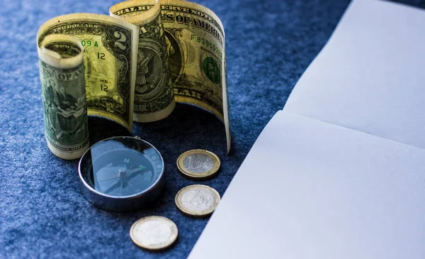 Dolar banknotları ve pusula ile Avro sikkeleri siyah masa arkaplanında not defteri beyaz kağıt 