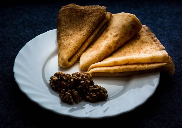 Koyu arkaplanda beyaz bir tabakta soyulmuş cevizli ev yapımı krepler. 