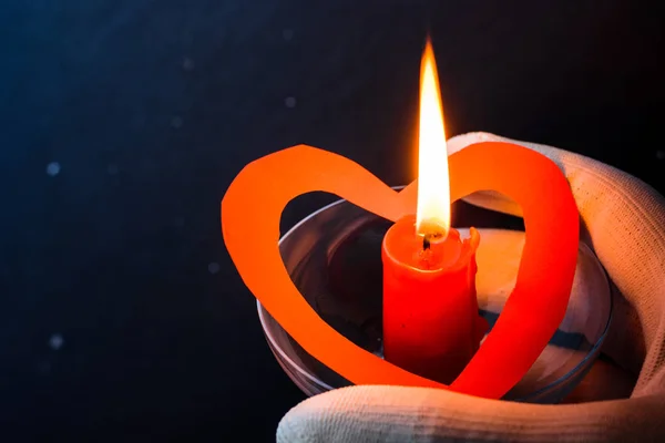 red candle in the shape of heart in hand with white gloves 