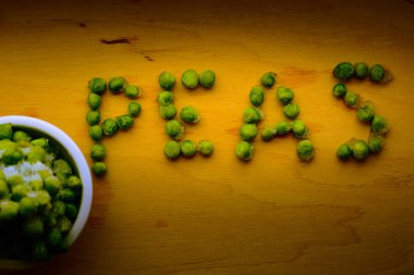 Tahta masadaki bezelyelerin yazılı olduğu bir kasede donmuş yeşil bezelyeler.