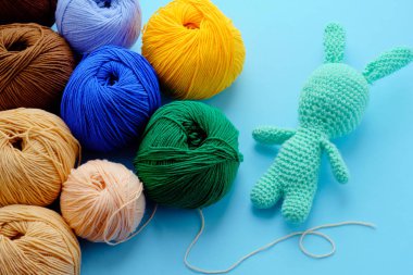 Mavi arka planda pastel yeşili doldurulmuş tavşan desenli parlak renk iplik demetleri. Amigurumi oyuncağı yapma kavramı, el işi, örgü, hobi