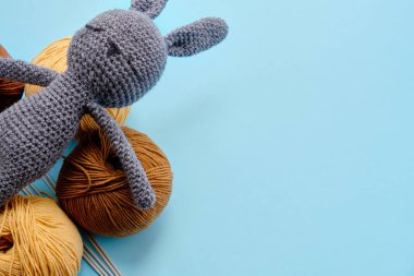 Mavi arka planda gri doldurulmuş amigurumi tavşanı olan parlak renk ipliklerinin üst görüntüsü. Amigurumi oyuncağı yapma kavramı, el işi, örgü, hobi