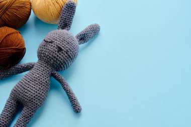 Mavi arka planda gri doldurulmuş amigurumi tavşanı olan parlak renkli iplik demetleri. Amigurumi oyuncağı yapma kavramı, el işi, örgü, hobi