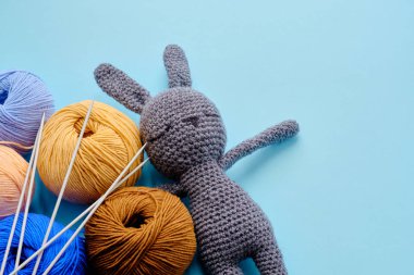 Mavi arka planda gri doldurulmuş tavşan ve iğneler olan renkli iplik demetleri. Amigurumi oyuncağı yapma kavramı, el işi, örgü, hobi