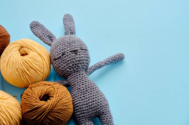 Mavi arka planda gri doldurulmuş amigurumi tavşanı olan parlak renkli iplik demetleri. Amigurumi oyuncağı yapma kavramı, el işi, örgü, hobi
