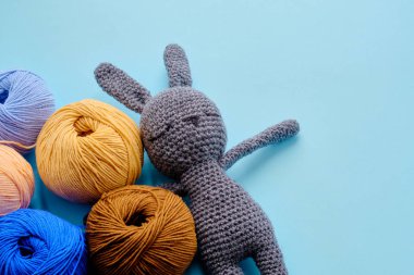 Mavi arka planda gri doldurulmuş amigurumi tavşanı olan parlak renkli iplik demetleri. Amigurumi oyuncağı yapma kavramı, el işi, örgü, hobi