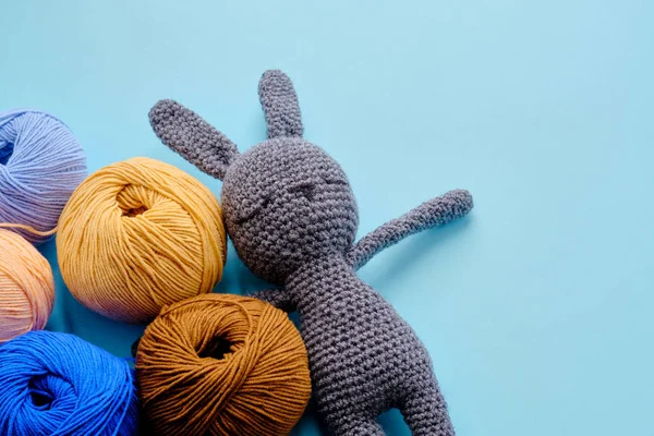 Mavi arka planda gri doldurulmuş amigurumi tavşanı olan parlak renkli iplik demetleri. Amigurumi oyuncağı yapma kavramı, el işi, örgü, hobi