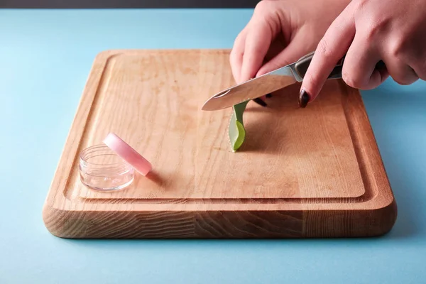 Pembe kapaklı, mavi arka planlı boş bir kutunun yanında bir bıçakla aloe vera dilimleri kesiyorum.