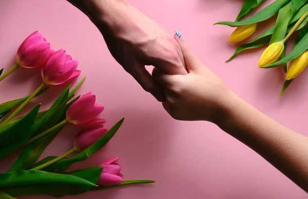 Держась за руки мужчины и женщины, на розовом фоне с тюльпанами, вид сверху вниз — стоковое фото