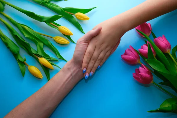 Держаться за руки на синем фоне с тюльпанами, вид сверху, праздничная концепция — стоковое фото