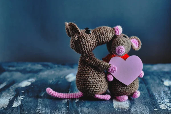 Handcrafted amigurumi rat hugs another knitted toy rat that holds the pink heart as a present. Valentine day, February 14, love, relations concept