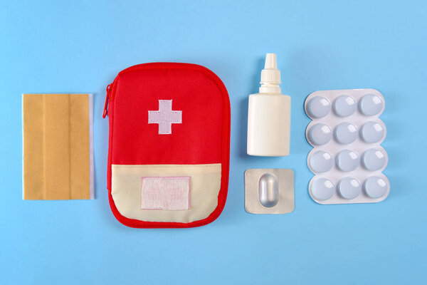 Закрытая туристическая аптечка скорой помощи рядом с таблетками, клейкие бинты и назальный спрей на ярко-голубом фоне
