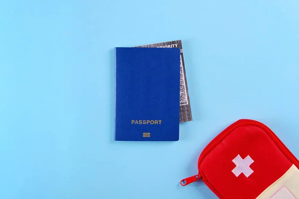 Синий внешний паспорт с билетом на самолет внутри и красная сумка аптечки на ярко-голубом фоне — стоковое фото