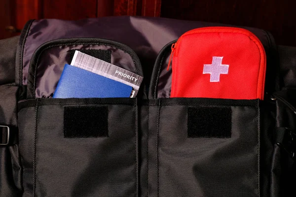 Pasaporte externo con billete de avión en el interior y kit de primeros auxilios para turistas en los bolsillos de la mochila de viaje —  Fotos de Stock