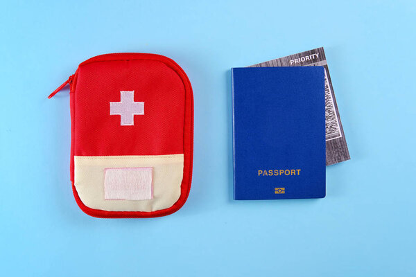 Blue external passport with airplane ticket inside and red travel first aid kit pouch on the bright blue background