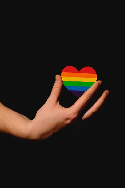 Braços femininos segurando o coração colorido em cores de orgulho LGBT no fundo escuro. Conceito do Dia Internacional Contra a Homofobia conceito, igualdade sexual, feminismo, segurança social e protetio — Fotografia de Stock