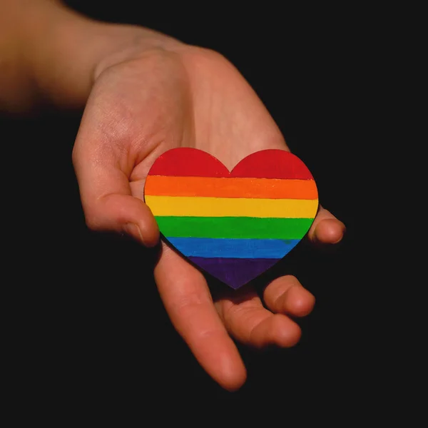 Braços femininos segurando o coração colorido em cores de orgulho LGBT no fundo escuro. Conceito do Dia Internacional Contra a Homofobia conceito, igualdade sexual, feminismo, segurança social — Fotografia de Stock