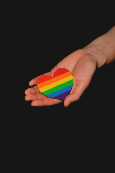 Female arm holding the heart coloured in LGBT pride colours on the dark background. Concept of the International Day Against Homophobia concept, sexual equality, feminism, social safety — Stock Photo, Image