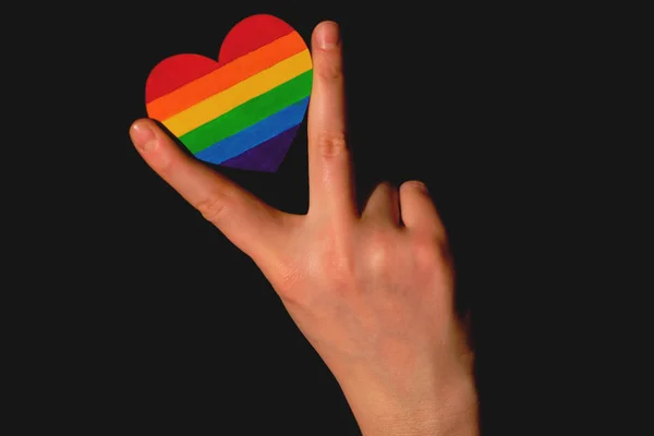 Braccia femminili che reggono il cuore colorato di colori dell'orgoglio LGBT sullo sfondo scuro. Concetto della Giornata internazionale contro l'omofobia concetto, uguaglianza sessuale, femminismo, sicurezza sociale e protectio — Foto Stock