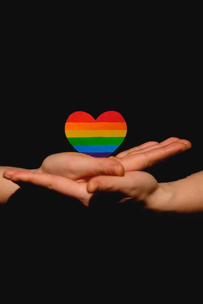 Female arms holding the heart coloured in LGBT pride colours on the dark background. Concept of the International Day Against Homophobia concept, sexual equality, feminism, social safety — 스톡 사진