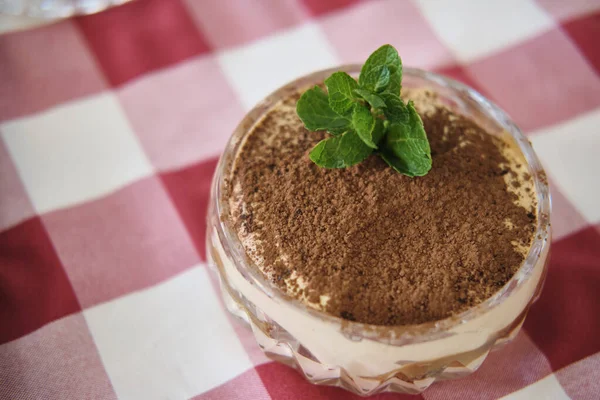 Kırmızı ve beyaz kareli arka planda bir bardakta klasik tiramisu mırıltılı tatlı.